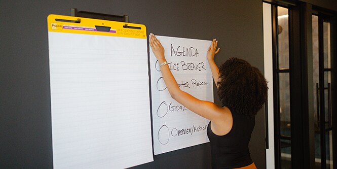Woman setting up Post-it® Meeting Chart with agenda and ice breaker details in a conference room
